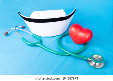 Stethoscope, Nurse Hat And Heart Red Ceramic On Blue Fabric.