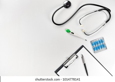 Stethoscope In The Office Of Doctors.Top View Of Doctor's Desk Table, Blank Paper On Clipboard With Pen. Copy Space. Designer's Blank