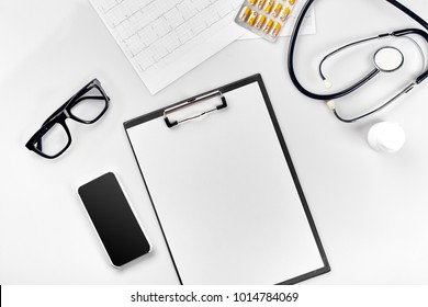 Stethoscope In The Office Of Doctors.Top View Of Doctor's Desk Table, Blank Paper On Clipboard With Pen. Copy Space. Designer's Blank