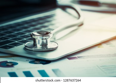 Stethoscope On Computer With Test Results In Doctor Consulting Room Background And Report Chart For Medical Costs In Modern Hospital On Laptop Desk. Healthcare Costs Business, Fees Concept. Gray Tone