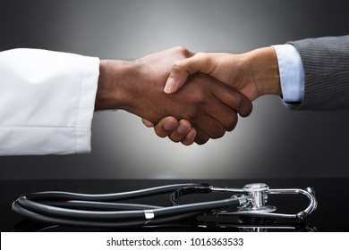 Stethoscope On Desk In Front Of The Doctor And Business Man Shaking Hands