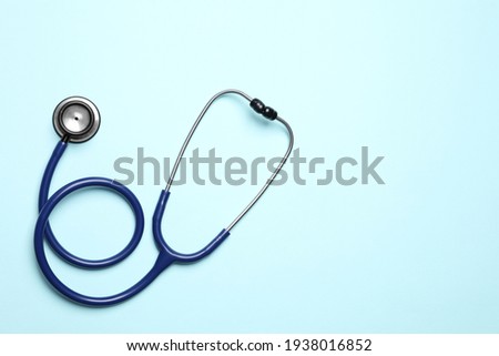Stethoscope on light blue background, top view. Space for text