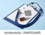 Stethoscope, pills, nasal spray and clipboard on light blue background, closeup. Medical tool