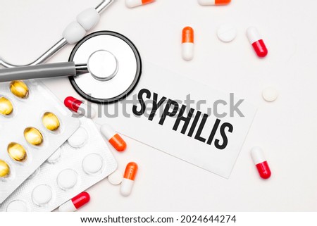 Stethoscope, pills and notebook with Syphilis word on medical desk.