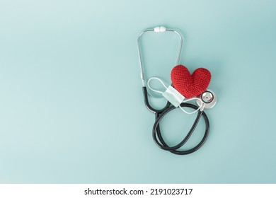 Stethoscope And Red Heart Shape And Face Mask Concept Of Health Care And Medical. Protect Heart With Surgical Mask Doctor And Hospital Equipment On Light Blue Background.