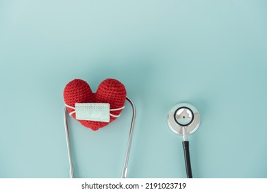 Stethoscope And Red Heart Shape And Face Mask Concept Of Health Care And Medical. Protect Heart With Surgical Mask Doctor And Hospital Equipment On Light Blue Background.