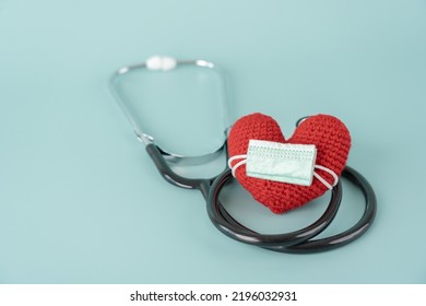 Stethoscope And Red Heart Shape And Face Mask Concept Of Health Care And Medical. Protect Heart With Surgical Mask Doctor And Hospital Equipment On Light Blue Background.