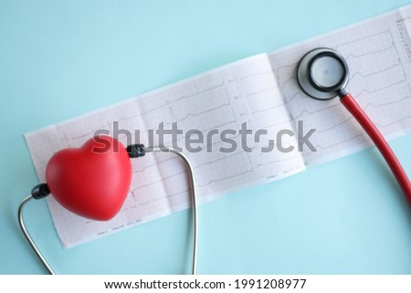 Stethoscope and red toy heart lying on electrocardiogram on blue background closeup