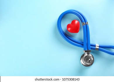Stethoscope and small red heart on color background. Heart attack concept