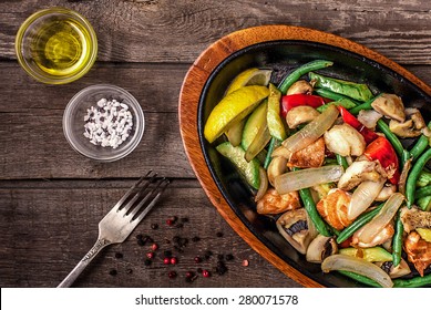 Stew chicken with vegetables and mushrooms on a wooden table with fork, pepper, salt, olive oil Foto Stok