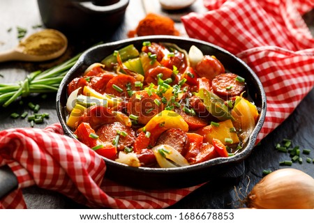 Stew with peppers and sausage in a cast iron skillet on a black background, close up. Traditional Hungarian dish called lecho