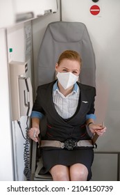 Stewardess In Medical Mask Fastening Seatbelt In Airplane