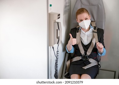 Stewardess In Medical Mask Sitting In Chair In Airplane Cabin