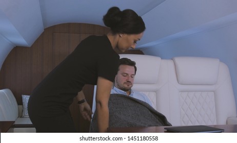 Stewardess Taking Care Of Passenger. Flight Attendant Covering Tired Sleepy Businessman With Blanket During Trip On Private Business Jet.