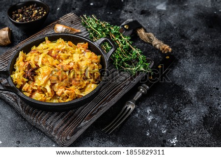 Stewed cabbage Bigos with mushrooms and sausages. Black background. Top view. Copy space