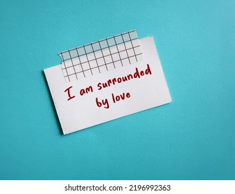 Stick Note On Blue Background With Red Handwritten Text - I Am Surrounded By Love - Positive Affirmation To Boost Self Esteem And Self Love In Daily Life, Overcome Negative Thoughts