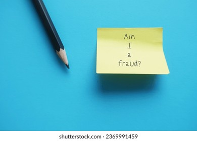 Stick note on blue background with text AM I A FRAUD? concept of IMPOSTER SYNDROME, feeling of doubt one own skills, talents or accomplishments and have internalized fear of being exposed as fraud