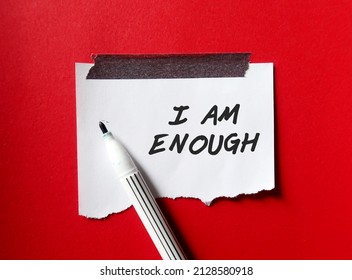 Stick note on red background with pen writing text I AM ENOUGH, Positive mantra affirmation self acceptance, Knowing that you are worthy, valid loved. Embrace all flaws and imperfection