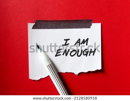 Stick note on red background with pen writing text I AM ENOUGH, Positive mantra affirmation self acceptance, Knowing that you are worthy, valid loved. Embrace all flaws and imperfection