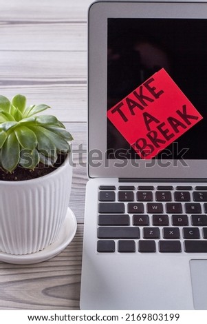 Sticker note with take a break message on laptop screen. Flowerpot with green leaves.