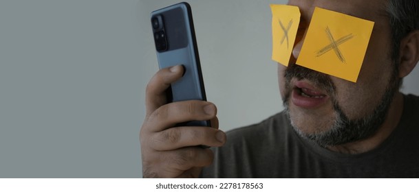 Stickers with painted crosses are glued to the eyes of a guy, a man is looking in a mobile cell phone with glued eyes, an isolated white background. shocked face - Shutterstock ID 2278178563