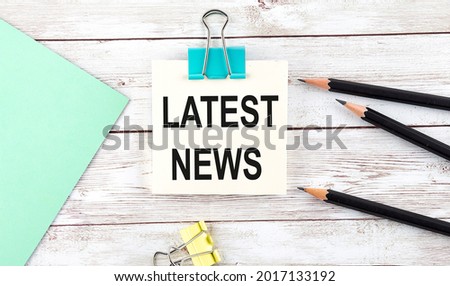 Stickers with pencils and notebook with text LATEST NEWS on the wooden background
