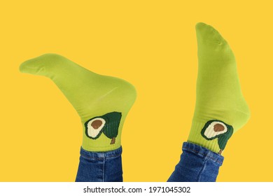 sticking up legs dressed in green socks with avocado pattern, on yellow background, concept