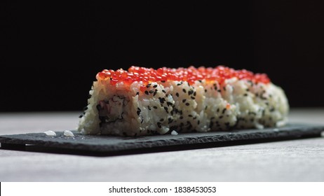 Sticks Take Sushi From Sushi Box. Variety Of Types Sushi With Red Caviar, Fish, Philadelphia Cheese And Chopsticks Close-up. Set Of Delicious Japanese Sushi Rolls On A Stone Board On A Black