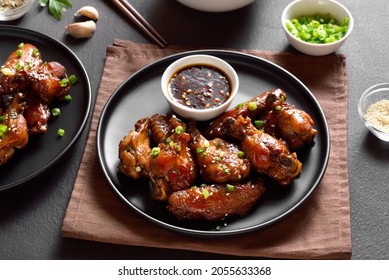 Sticky honey-soy chicken wings on plate over dark stone background. 
