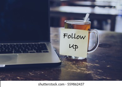 Sticky note with FOLLOW US wording on glass of tea with laptop on wooden table. Motivation and positive wishes concept
