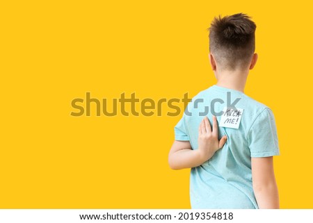 Sticky note with text KICK ME on back of little boy against color background. April Fools Day prank