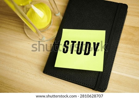Sticky note with the word STUDY on a black notebook beside an hourglass, symbolizing learning, education, productivity, time management, and academic planning.