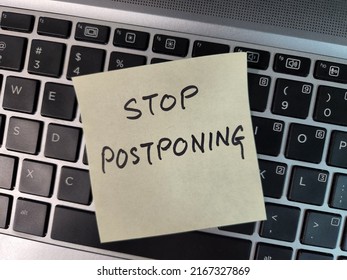 A sticky note with the words "Stop Postponing" written