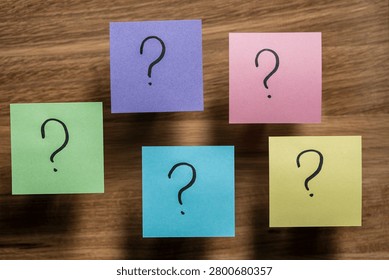 Sticky notes with question marks on wood background. Five multicolored post it papers with handwritten question marks. Conceptual image for choices, FAQ, problem solving, decision making or doubts