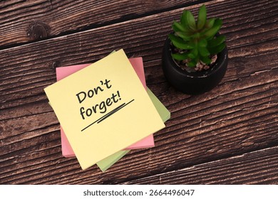 Sticky notes with the text Don't forget, placed on a wooden desk beside a small potted succulent, symbolizing reminders, organization, and productivity.

