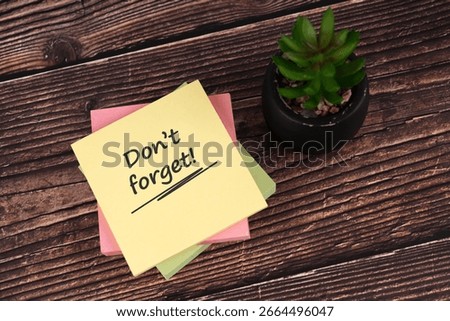 Sticky notes with the text Don't forget, placed on a wooden desk beside a small potted succulent, symbolizing reminders, organization, and productivity.

