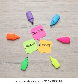 Sticky notes with words Diversity, Equality, Inclusion and markers on wooden table, flat lay