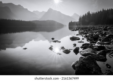 Still alpine lake reflecting sun and surrounding mountains and woods, monochromatic, Jasper NP, Canada