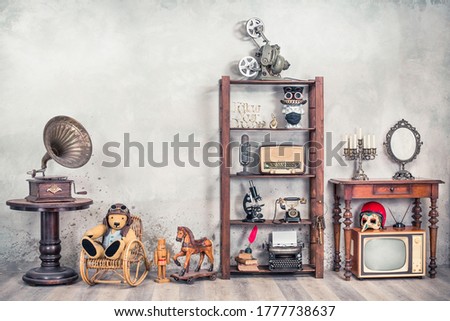 Still life with antique gramophone, old Teddy Bear, toy horse, collection of outdated media devices and writers tools, microscope, desk mirror front concrete background. Vintage style filtered photo