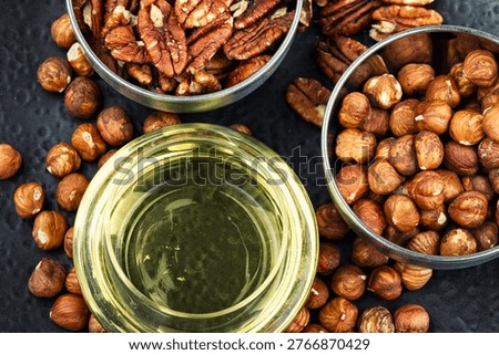 Still life of assorted nuts including hazelnuts and pecans served in metal bowls with a glass of golden oil