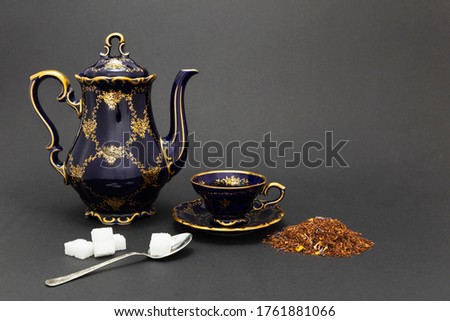 Still life with a beautiful cobalt blue colored vintage porcelain tea set with golden floral pattern, spoon with sugar cubes and dry tea leaves.
