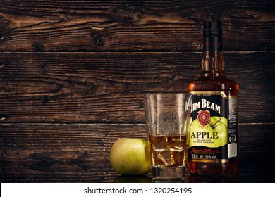 Still life with bottle of Jim Beam Apple (apple liqueur infused with kentucky straight bourbon), glass with bourbon, ice and green apple on a brown wooden background with copy space.