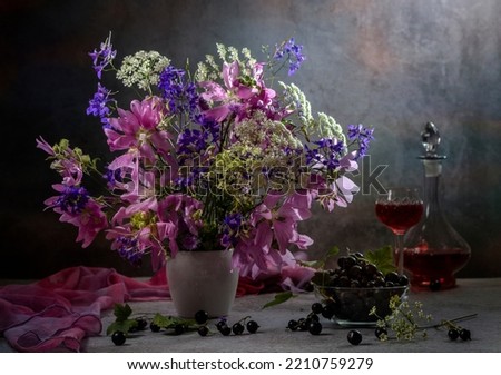 Still life with a bouquet of wild flowers and black currants on a dark background.