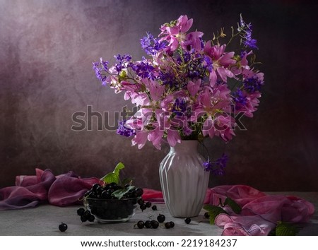 Still life with a bouquet of wild flowers and black currants on a dark background.