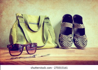 Still Life With Casual Woman, Shoes, Sunglasses, And Bag On Wooden Table Over Wall Background