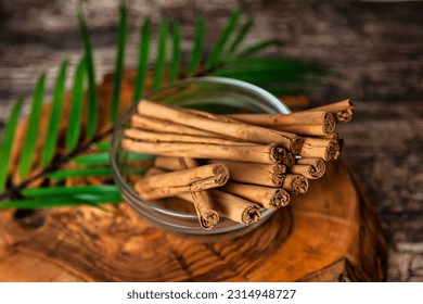Still life of cinnamon sticks in glass plate with palm leaf on wood board on table, top view. Rustic style of natural food of ceylon cinnamon sticks. Delicious healthy concept. Copy ad text space - Shutterstock ID 2314948727