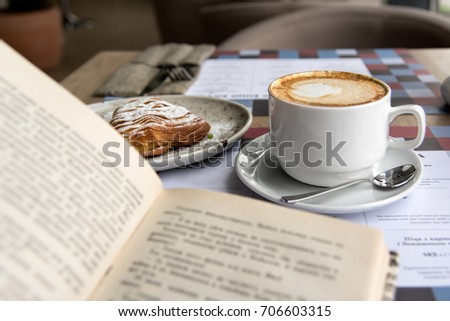 Still life details, cup of Cappuccino and cake with book on table in coffee shop cafe, shallow DOF.