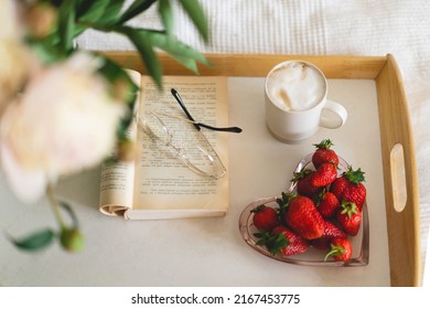 Still life details in home interior of living room. Open book with glasses, cup coffee, strawberries and bouquet white pink peonies flowers. Read and rest. Cozy home