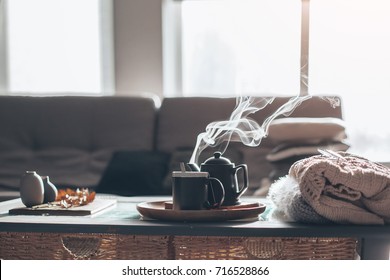 Still life details in home interior of living room. Sweaters and cup of tea with steam on a serving tray on a coffee table. Breakfast over sofa in morning sunlight. Cozy autumn or winter concept. - Shutterstock ID 716528866
