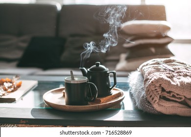 Still life details in home interior of living room. Sweaters and cup of tea with steam on a serving tray on a coffee table. Breakfast over sofa in morning sunlight. Cozy autumn or winter concept. - Shutterstock ID 716528869